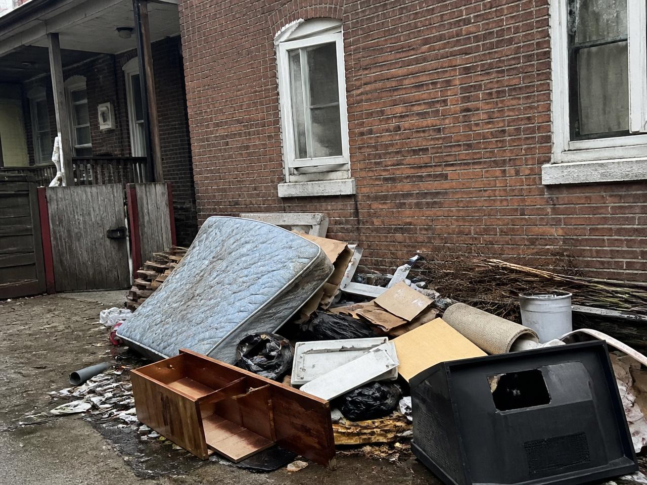 Baltimore rowhouse alley piled with junk, mattress and debris before Charm City Haulers cleanup